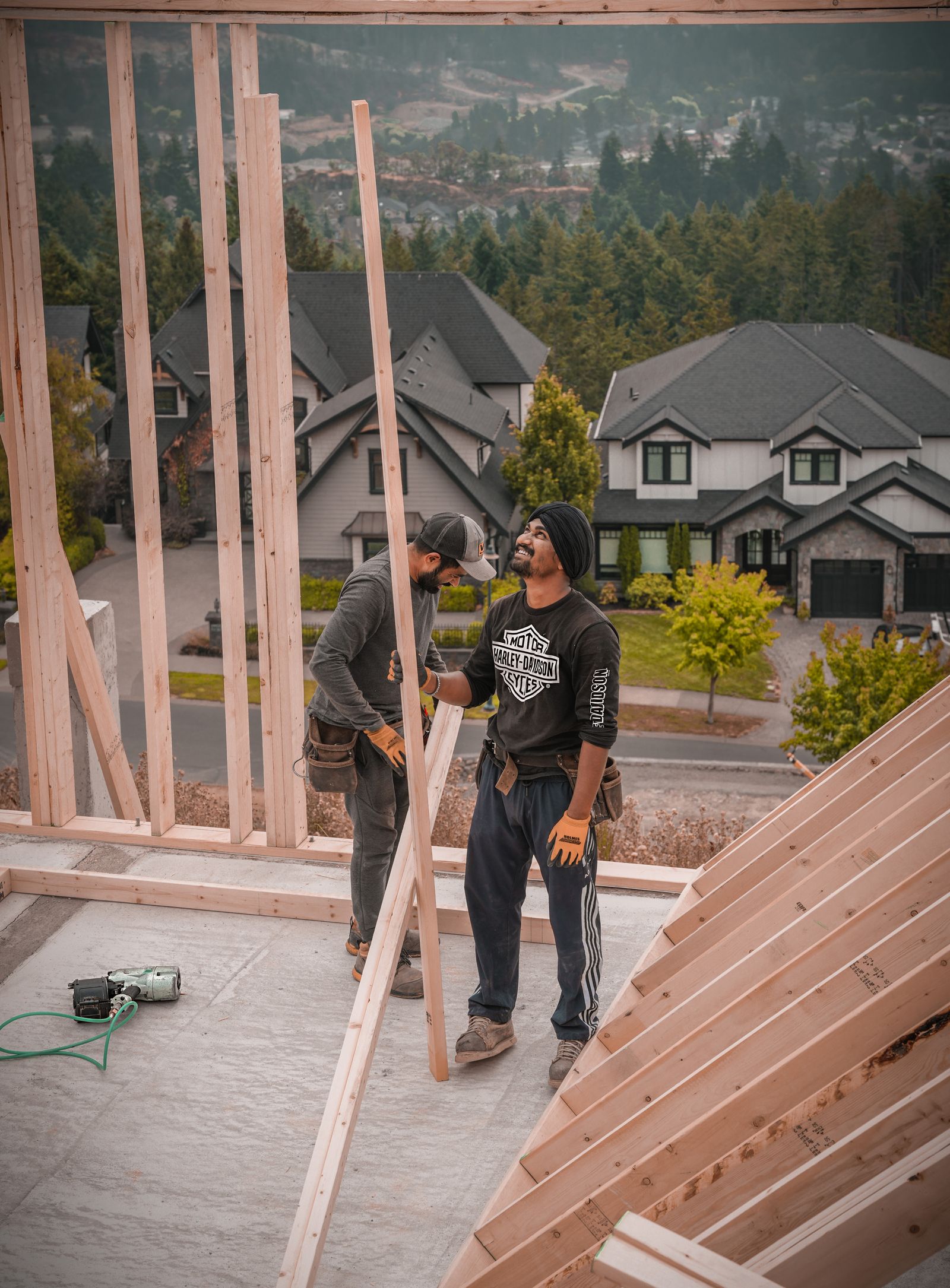 Two carpenters working on a framed structure with a neighborhood behind them