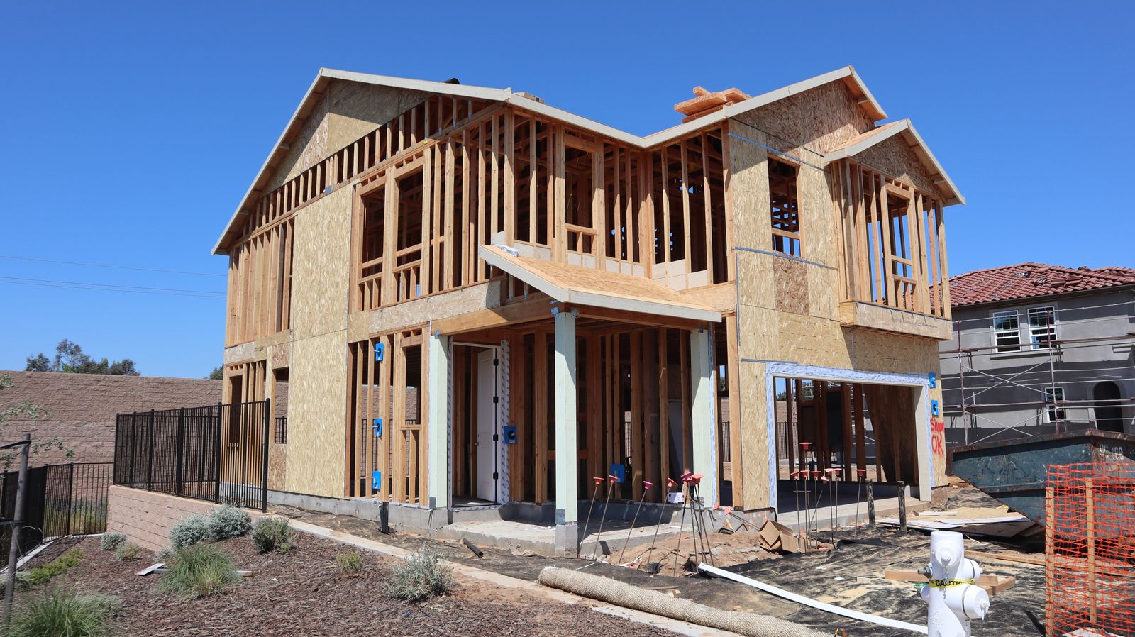 Two-story house under construction with full wood framing against a clear blue sky